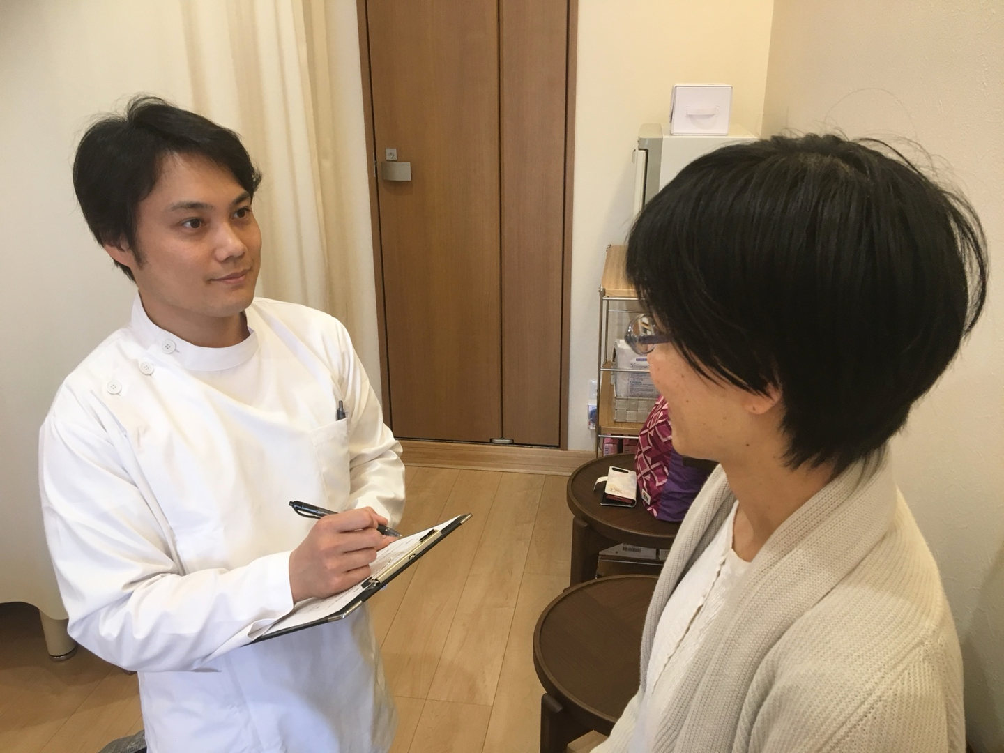院内で施術者が問診票を手に、座っている患者さんからお話を伺う様子
